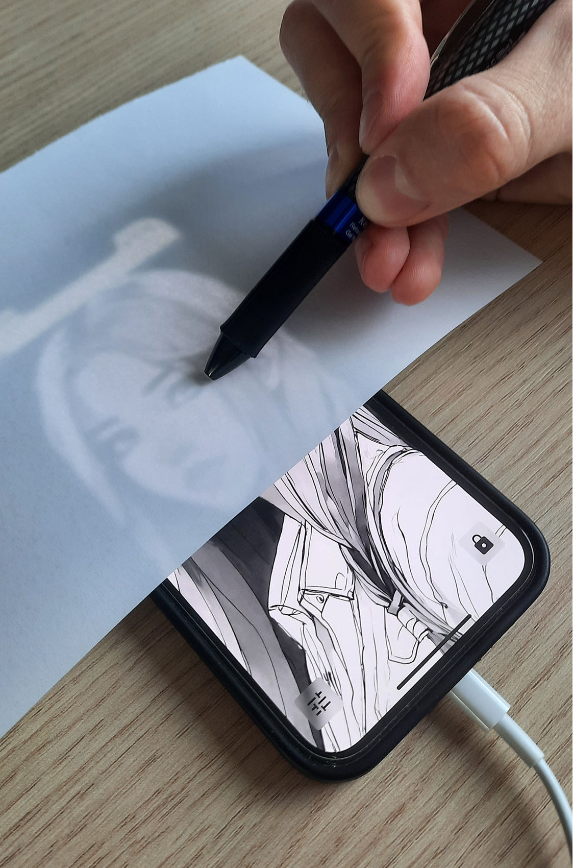 Hand tracing a drawing on paper placed over a phone running the Lightbox draw app